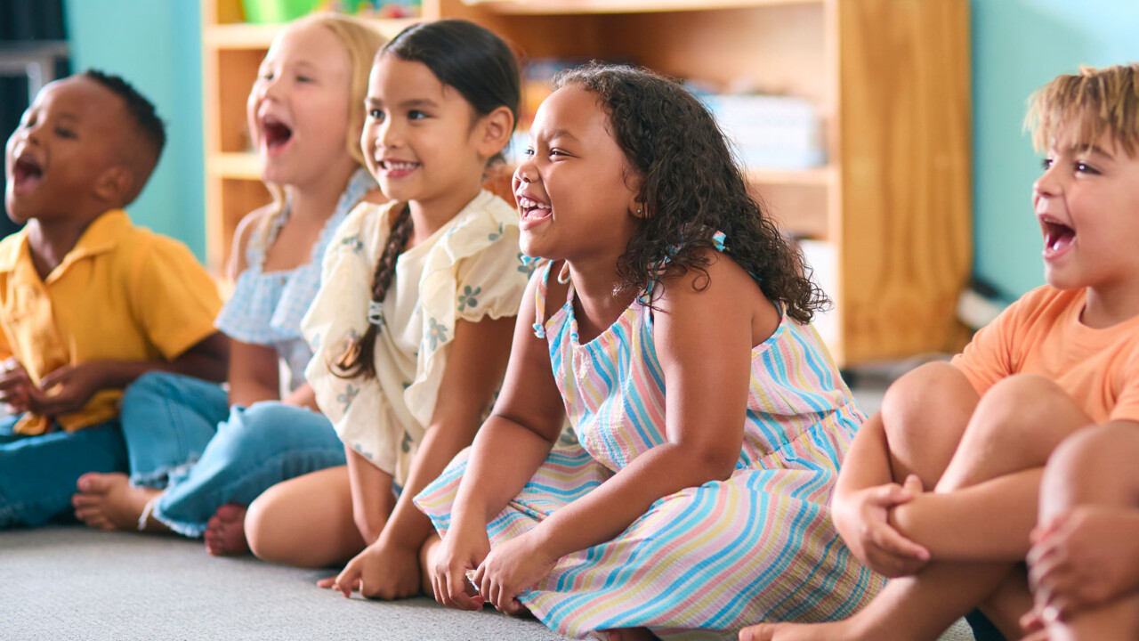 line of elementary children sitting on a floor in a classroom.