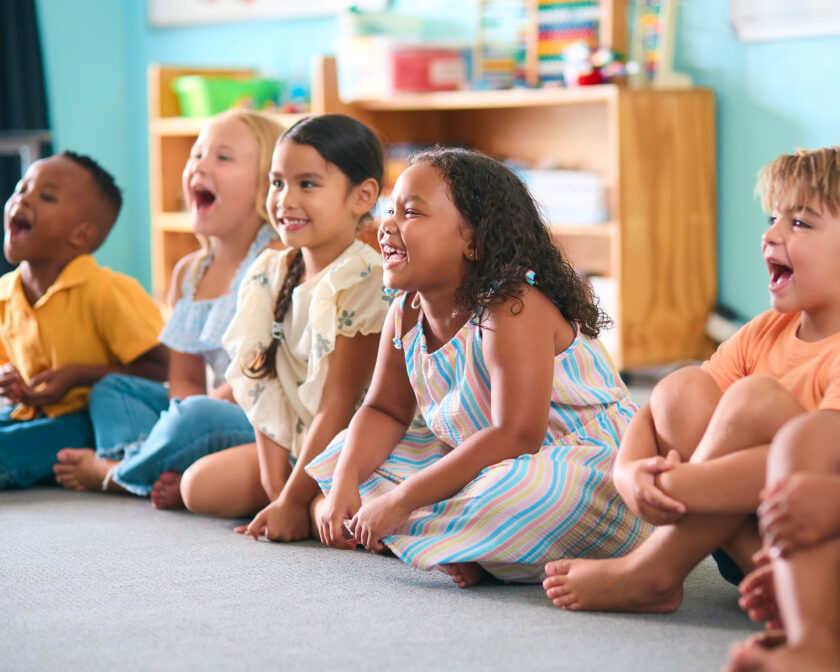 line of elementary children sitting on a floor in a classroom.